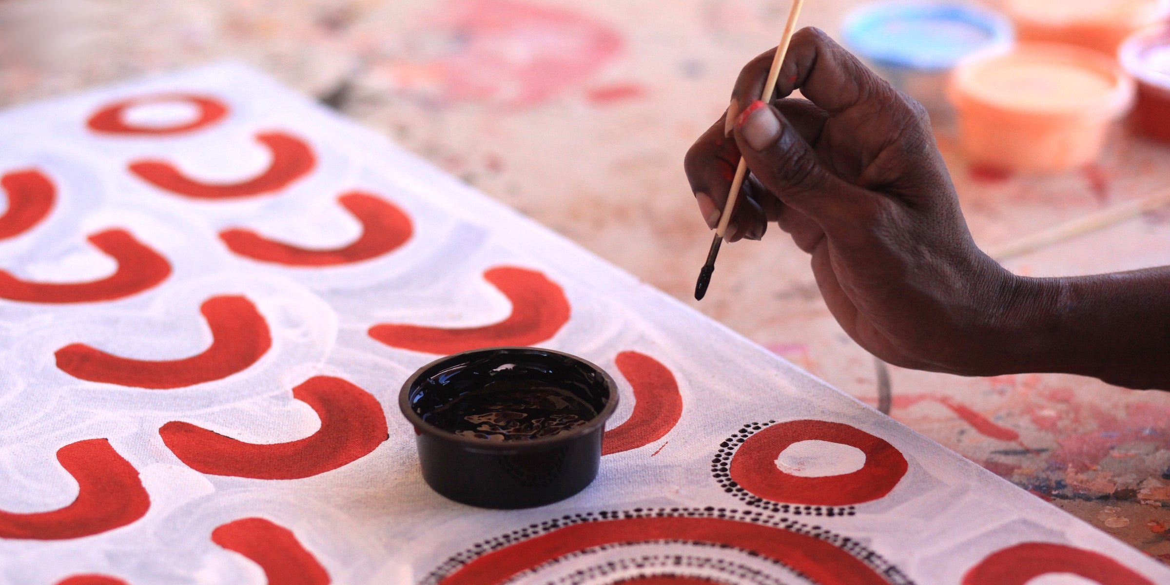 Hand wearing Indigenous designed cuff against a banner of Aboriginal art