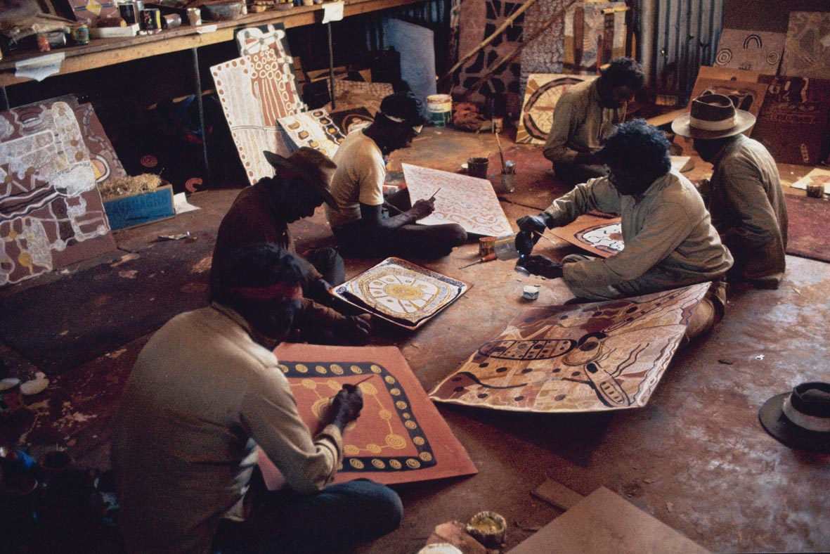 Early Papunya artists working under a shed in the Northern Territory